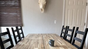 Una mesa de comedor con sillas negras, un cráneo de toro montado en la pared y una ventana con persianas.
