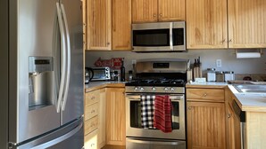 Una cocina con armarios de madera, electrodomésticos de acero inoxidable que incluyen un refrigerador, microondas y estufa, además de un dispensador de agua.