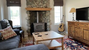 Una sala de estar acogedora con chimenea de piedra, un sofá, una mesa de centro, un televisor y una guitarra.