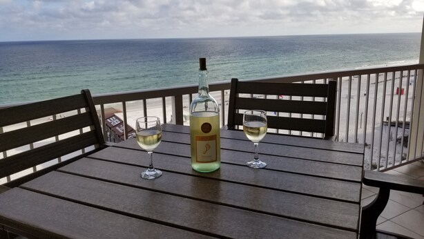 Une table avec deux verres de vin blanc et une bouteille de Riesling sur un balcon donnant sur l’océan.