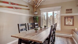 A dining room with a wooden table and chairs, a chandelier, skis on the wall, and a window with a view. - Gorgeous Luxury Townhome/Pool and Hot Tub Access (Keystone)