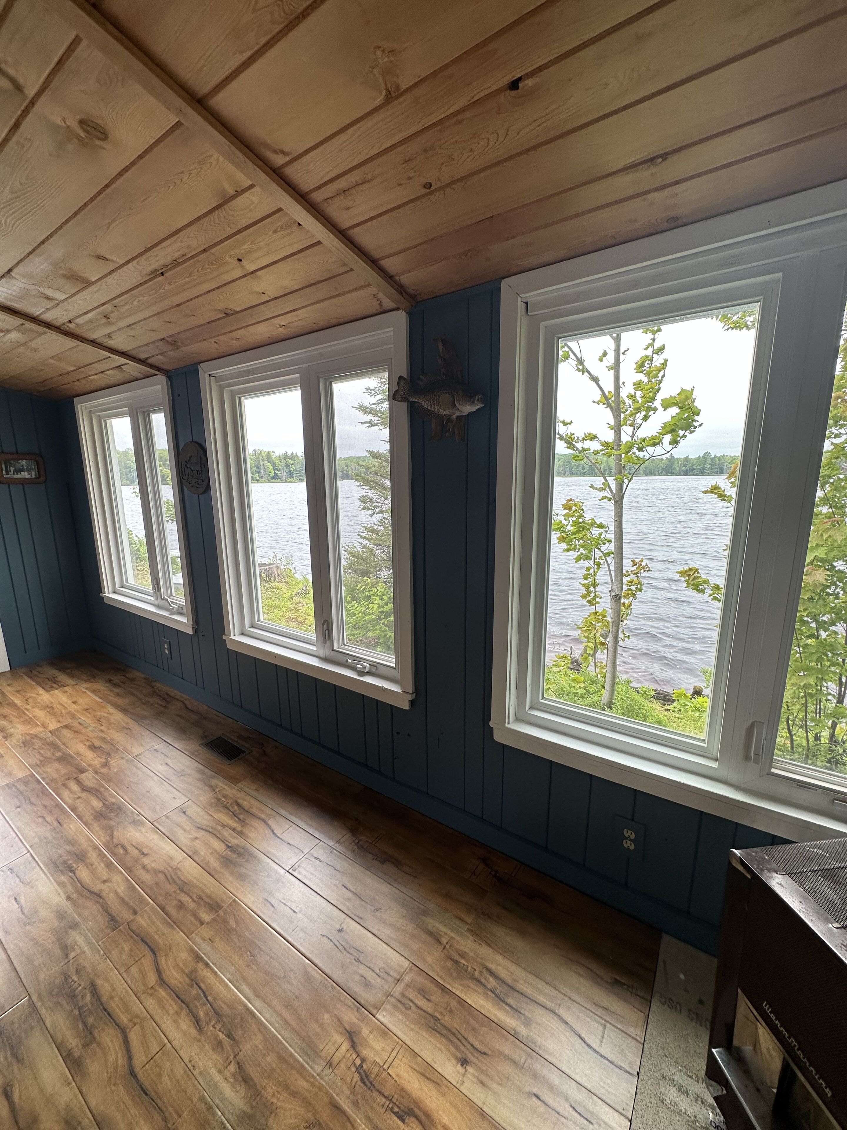 A room with wooden floors, blue walls, and large windows overlooking a body of water.
