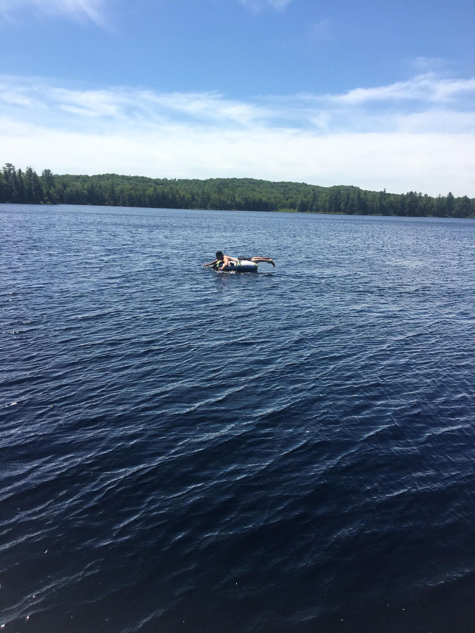 A person on a kayak in a large body of water with a forested shoreline in the background.