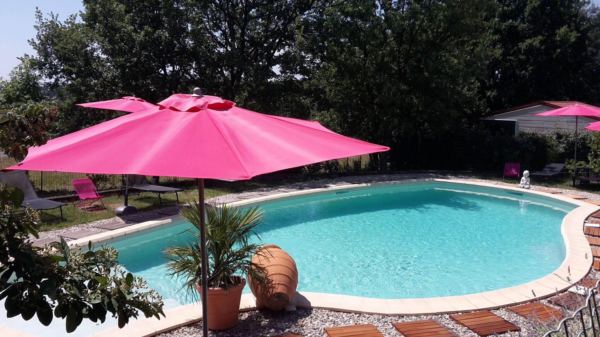 A swimming pool with pink umbrellas, surrounded by a wooden deck and potted plants.