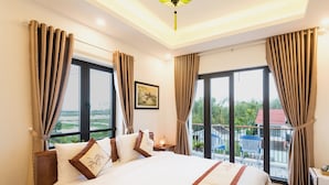 Habitación de hotel con una cama grande, dos ventanas con cortinas, una mesita de noche y vistas al exterior.
