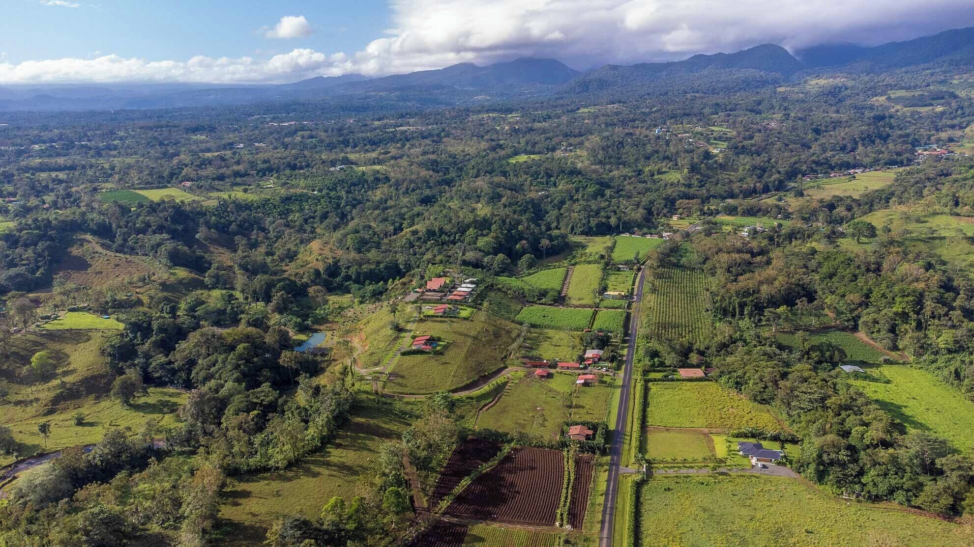Une vue aérienne d’un paysage rural, avec des champs, une route et quelques bâtiments dispersés.
