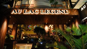 Der Eingang des Hotels Au Lac Legend mit einer auffälligen Beschilderung, umgeben von üppiger Bepflanzung und Zimmerpflanzen.