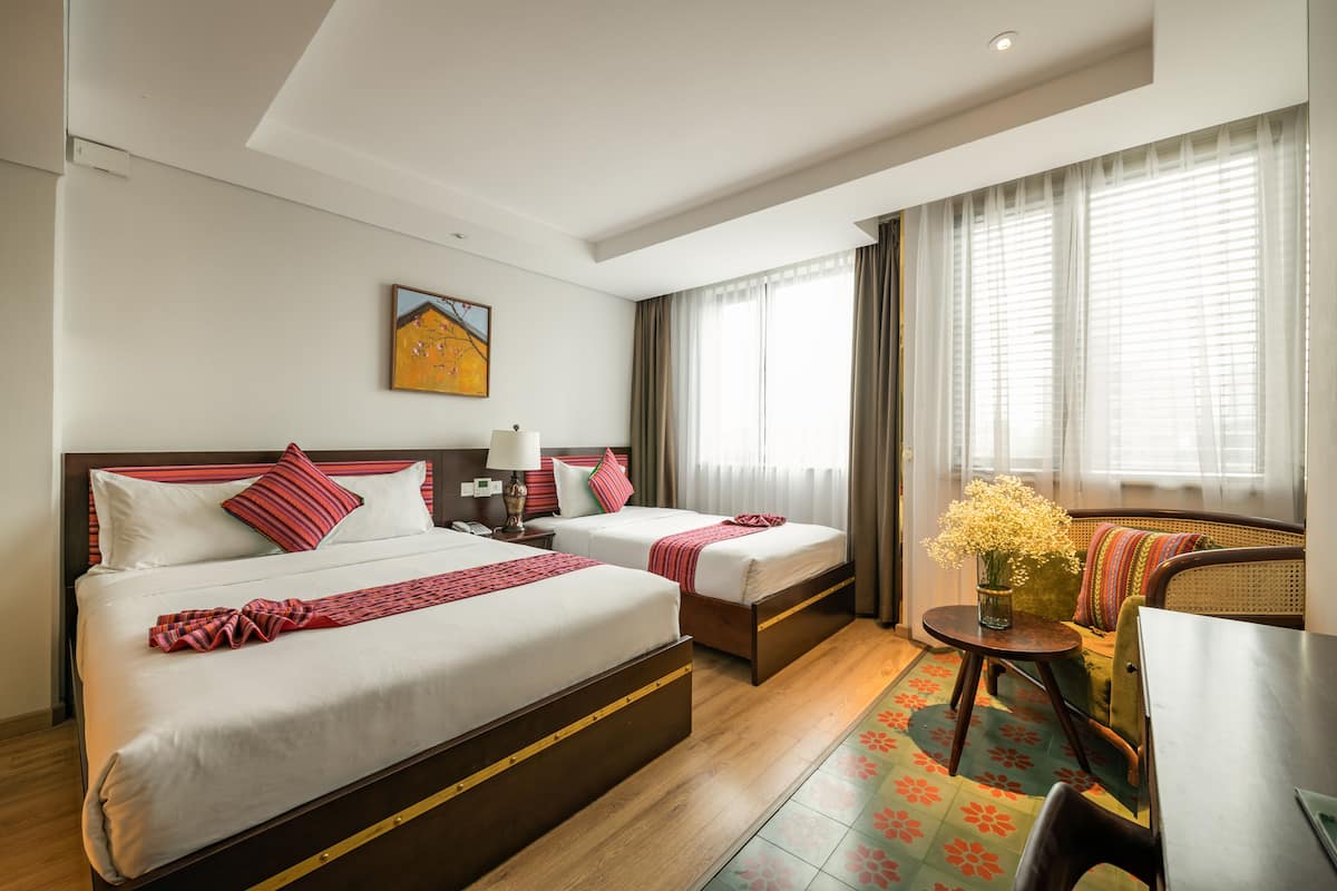Une chambre d’hôtel avec deux lits, un canapé, une petite table avec un vase et un tableau au mur.