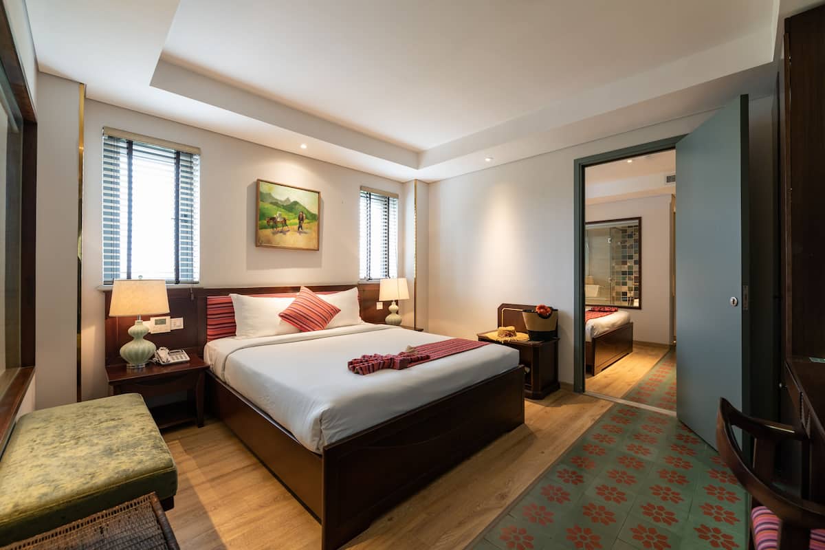 Une chambre d’hôtel moderne, dotée d’un grand lit, de tables de chevet, d’une petite table, d’une chaise et d’une salle de bain visible à travers une porte ouverte.