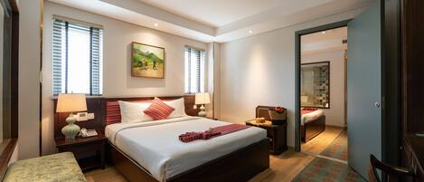 A modern hotel room with a large bed, bedside tables, a nightstand, a chair, and a bathroom visible through an open door.