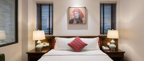 Habitación de hotel con una cama grande, dos mesitas de noche con lámparas, un sillón verde y un cuadro en la pared.