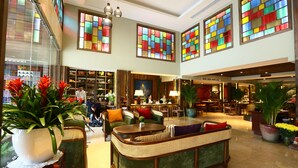 Eine großzügige Lobby mit hohen Decken, großen Fenstern mit bunten Glasverzierungen und gemütlichen Sitzbereichen.