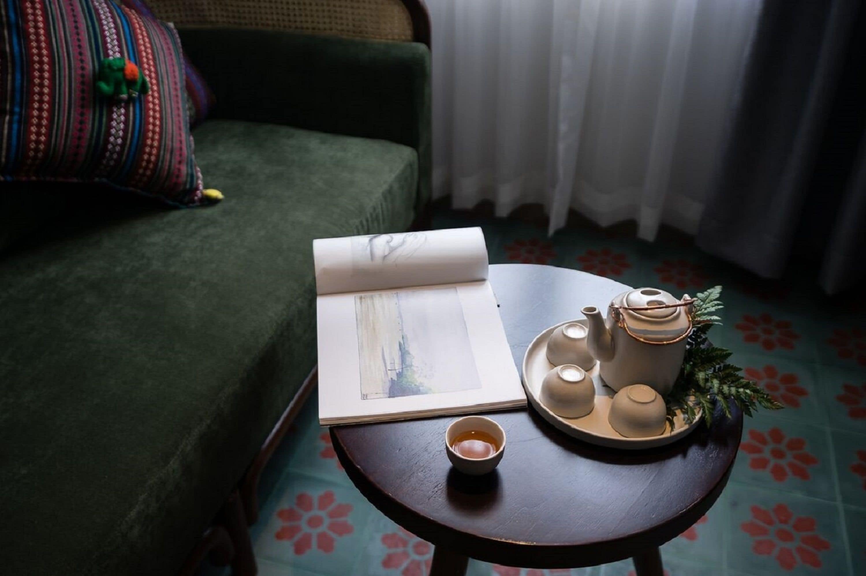 A cozy room with a green sofa, a small wooden table with a book, a teapot, cups, and a tray.
