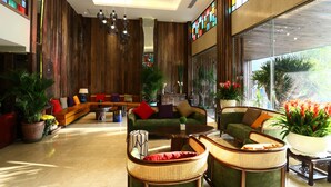Eine geräumige Lobby mit einem grünen Sofagarnitur, Korbstühlen und einem Couchtisch. Ücht Blumentöpfen und einem großen Fenster mit Blick.