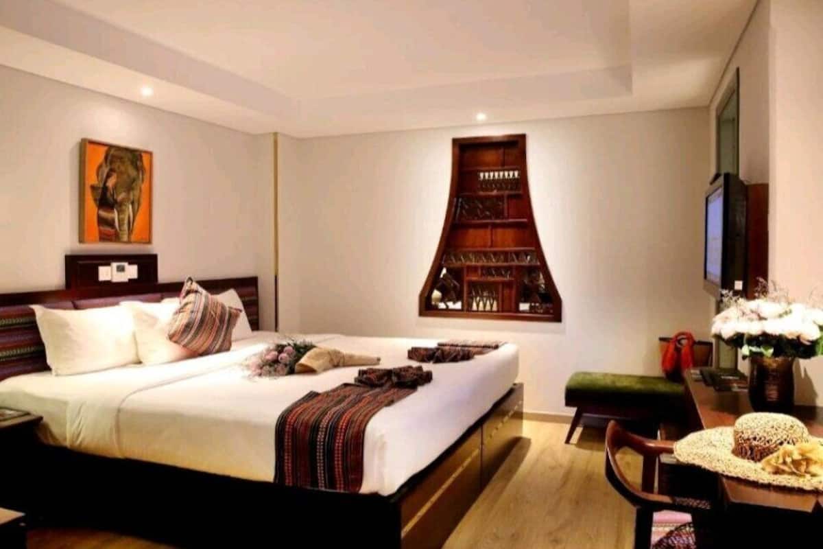 Une chambre d’hôtel avec un grand lit, une télévision, une bibliothèque et un bureau avec une lampe.