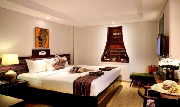 Una habitación de hotel con una cama grande, televisión, estantería y escritorio con lámpara.