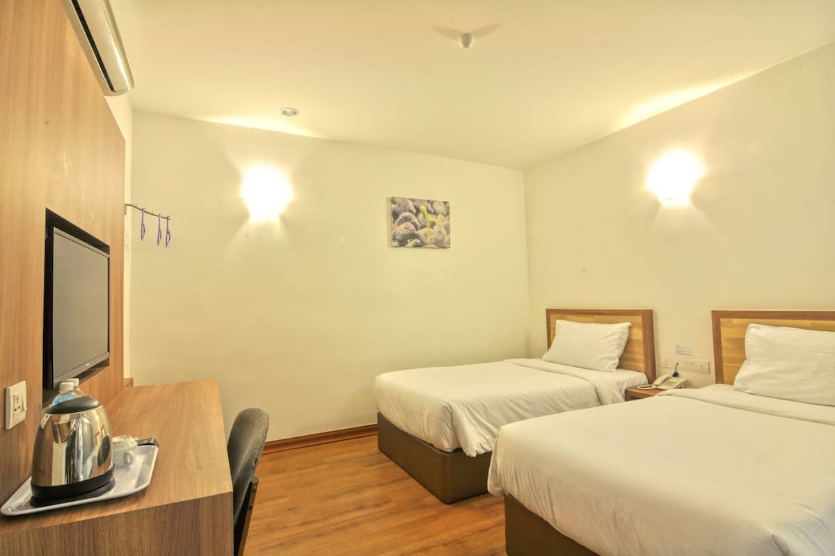 Une chambre d’hôtel avec deux lits, un bureau avec une machine à café, une télévision et un tableau au mur.