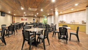 Een restaurant met houten balkenplafond en een betegelde spatwand. Tafels en stoelen staan klaar voor het dineren.