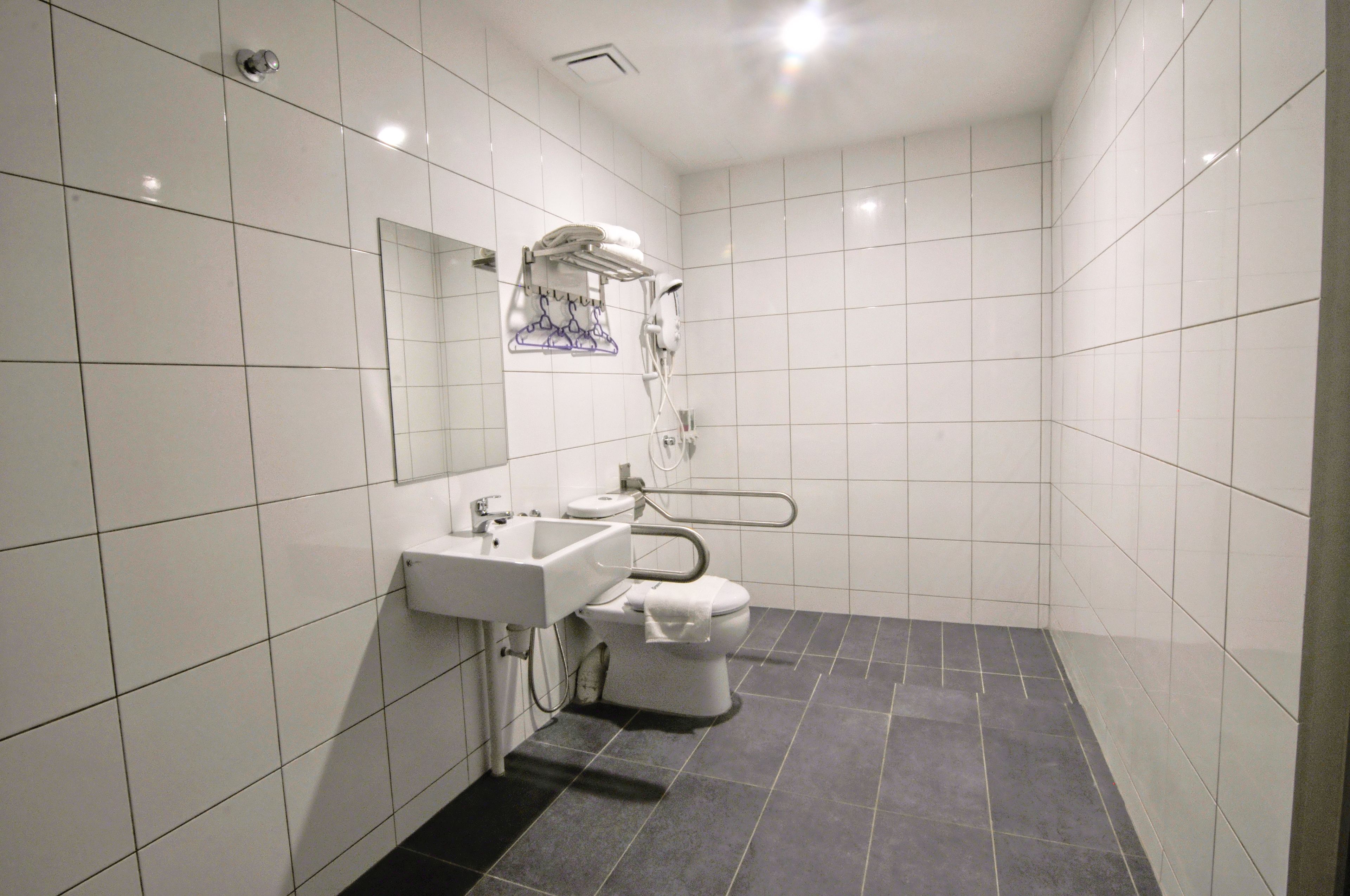 A modern bathroom with white tiles, a sink, a toilet, and a shower area.