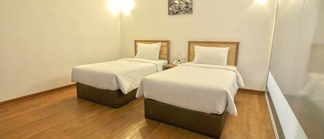 A hotel room with two beds, wooden flooring, and a painting on the wall.