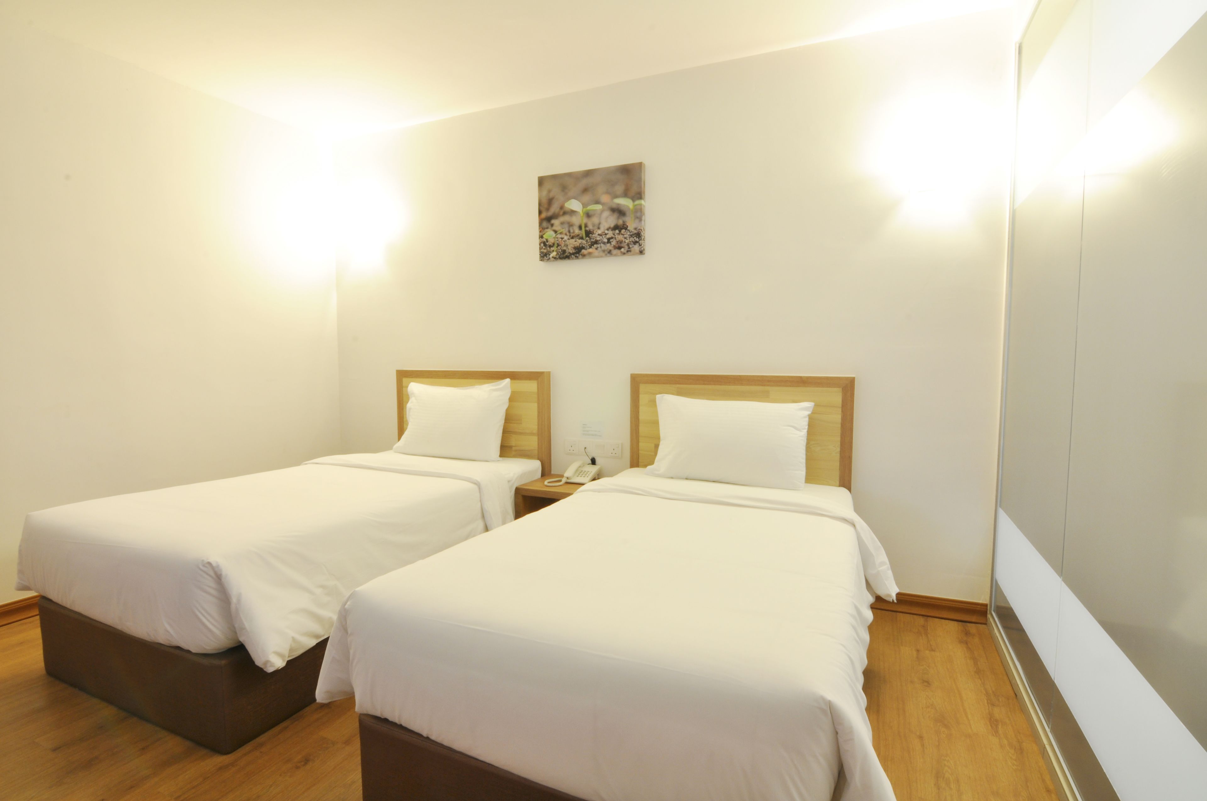 A hotel room with two single beds, a bedside table with a phone, and a small painting on the wall.
