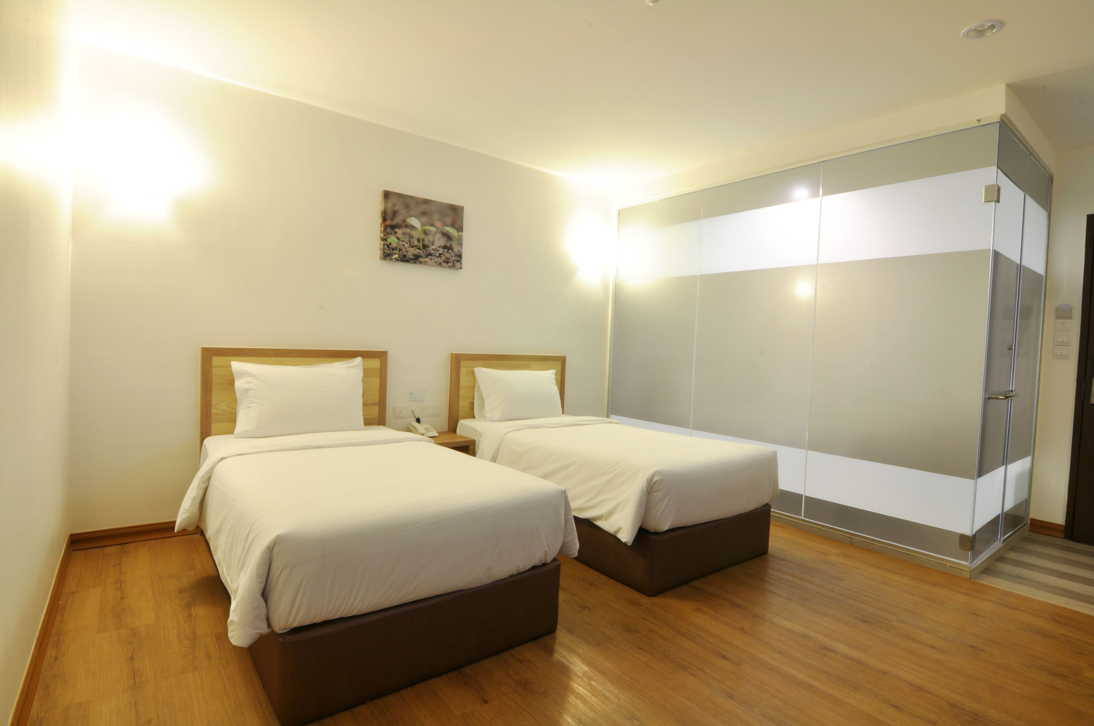Habitación de hotel con dos camas, suelo de madera, un espejo grande y un cuadro pequeño en la pared.