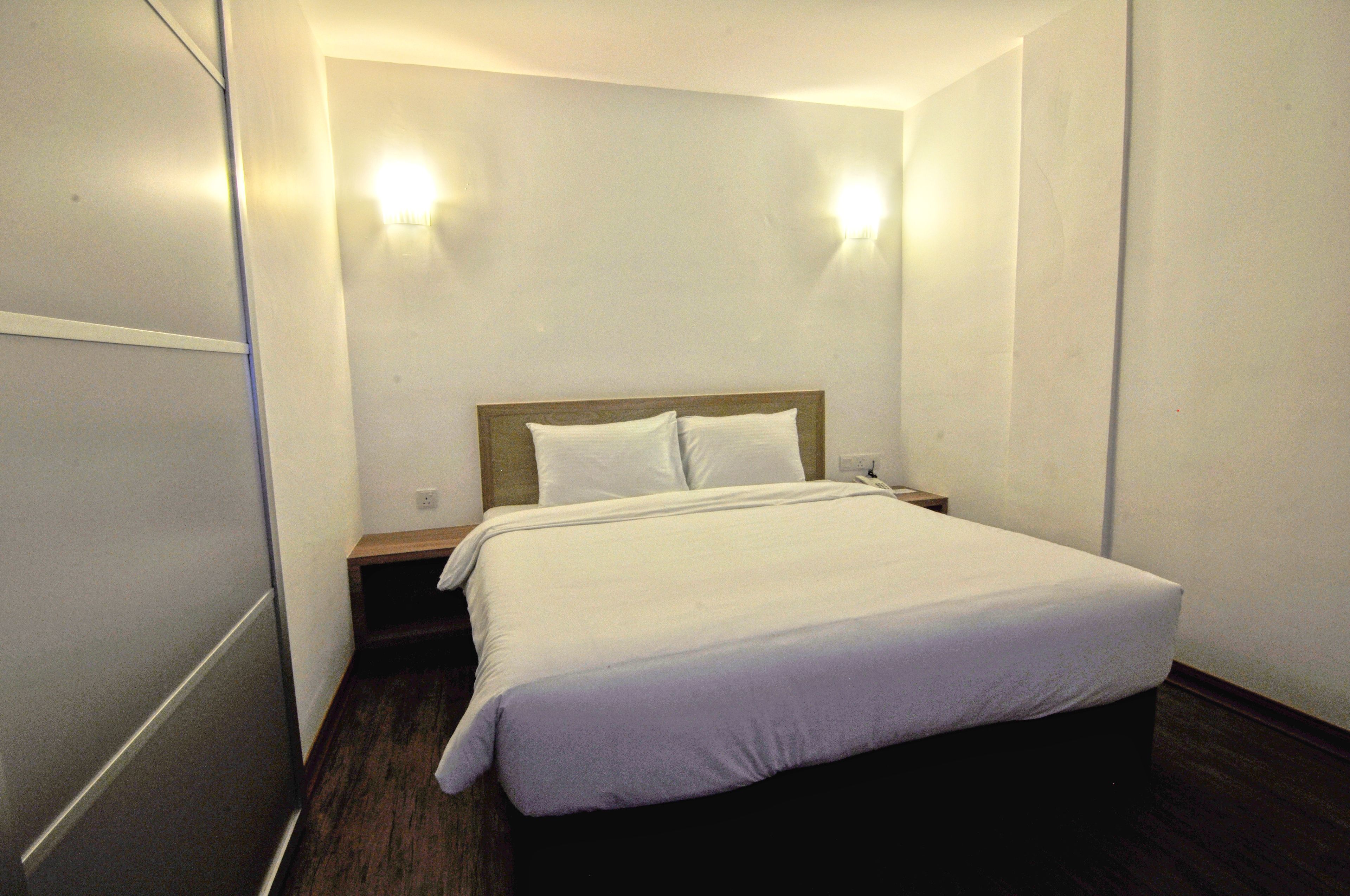 Una habitación de hotel con cama, mesita de noche y dos luces fijadas a la pared.