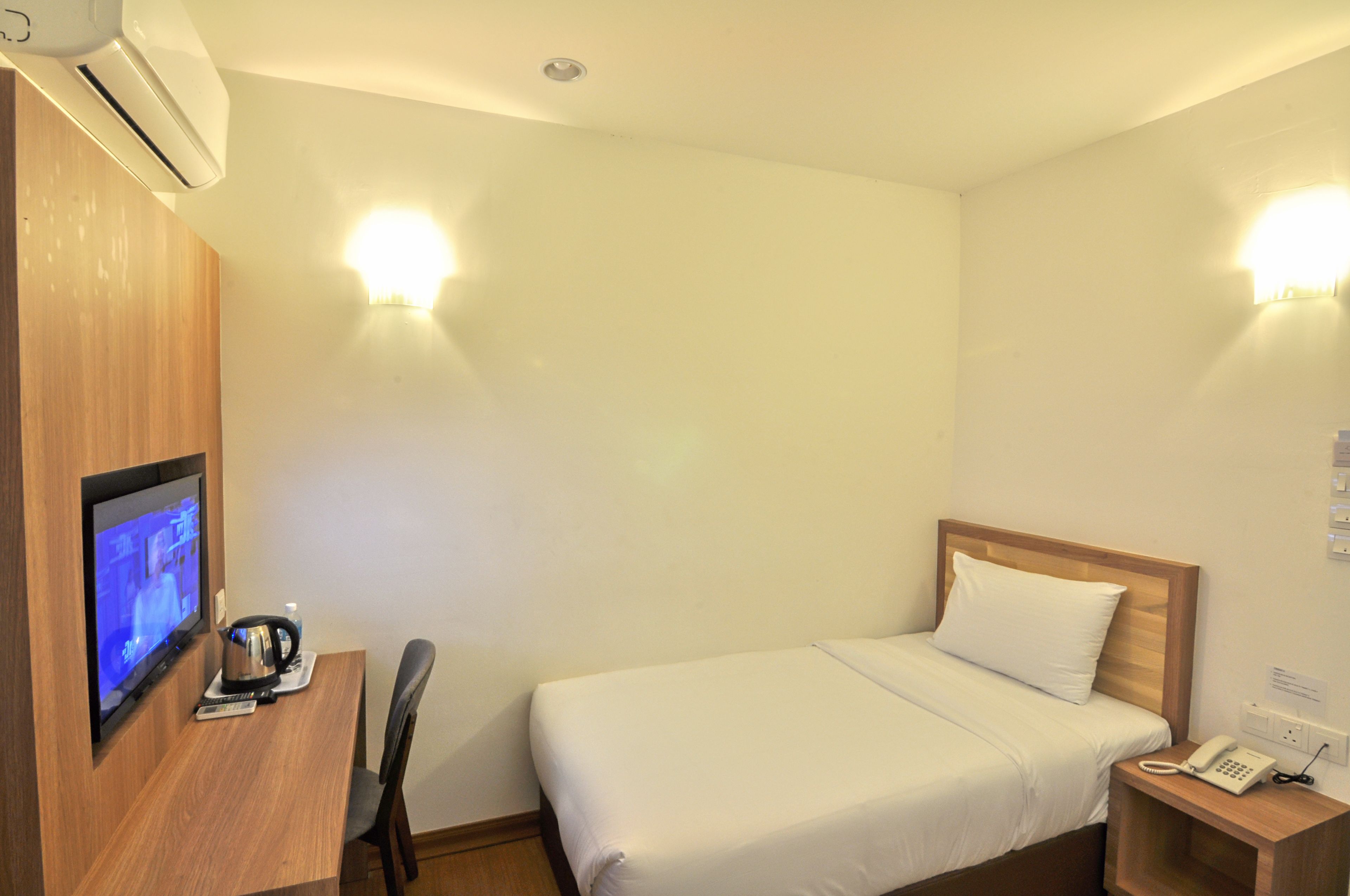 Une chambre d’hôtel comprenant un lit, une table de chevet, un téléviseur fixé au mur, un appareil de climatisation et un luminaire fixé au mur.