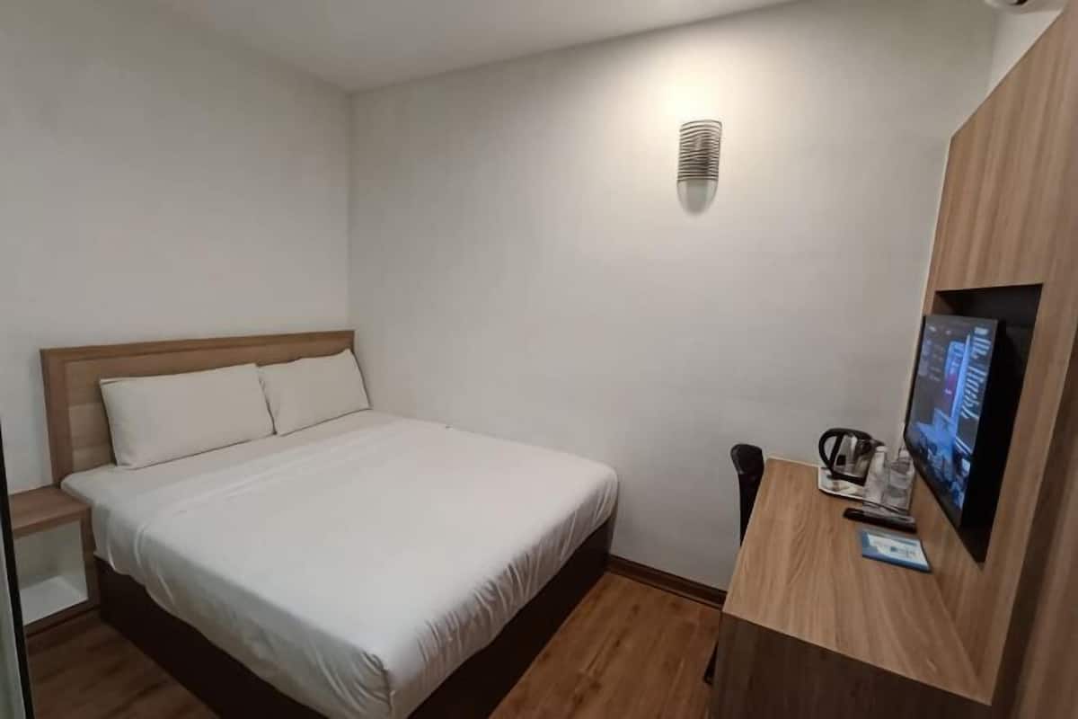 Une chambre à coucher avec un lit, un bureau avec un ordinateur, une chaise et un téléviseur posé sur une commode en bois.