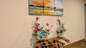 Een kamer met een houten tafel, twee vazen met bloemen, en een schilderij van een zonsondergang aan de muur.