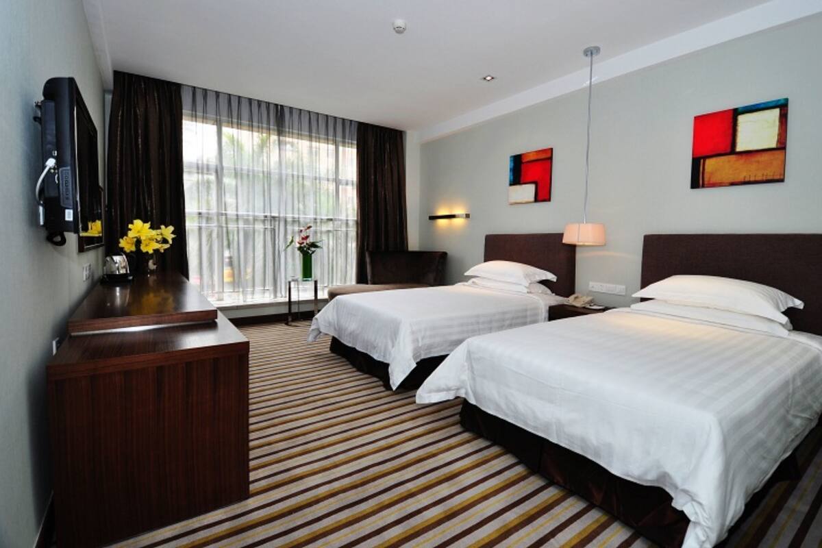 A hotel room with two beds, a desk, a chair, a TV, and a window with curtains.