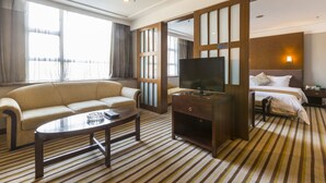 A hotel room with a sofa, a TV, a bed, and a striped carpet. - Poly Hotel (Guangzhou)