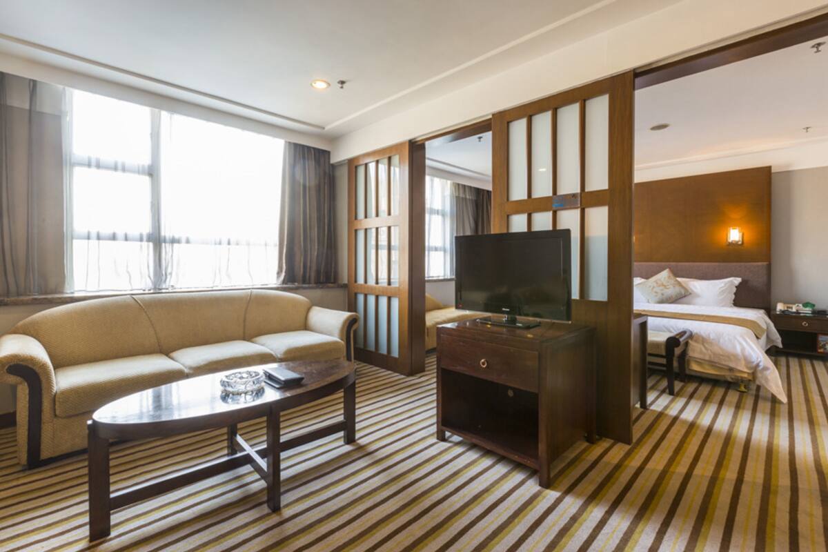 A hotel room with a sofa, a TV, a bed, and a striped carpet.