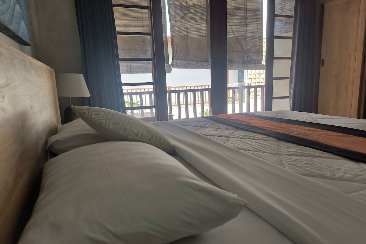 A hotel room with a bed, a nightstand, a lamp, and a view of the balcony.