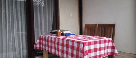 A small room with a table covered by a red and white checkered tablecloth, a chair, and a window with curtains.