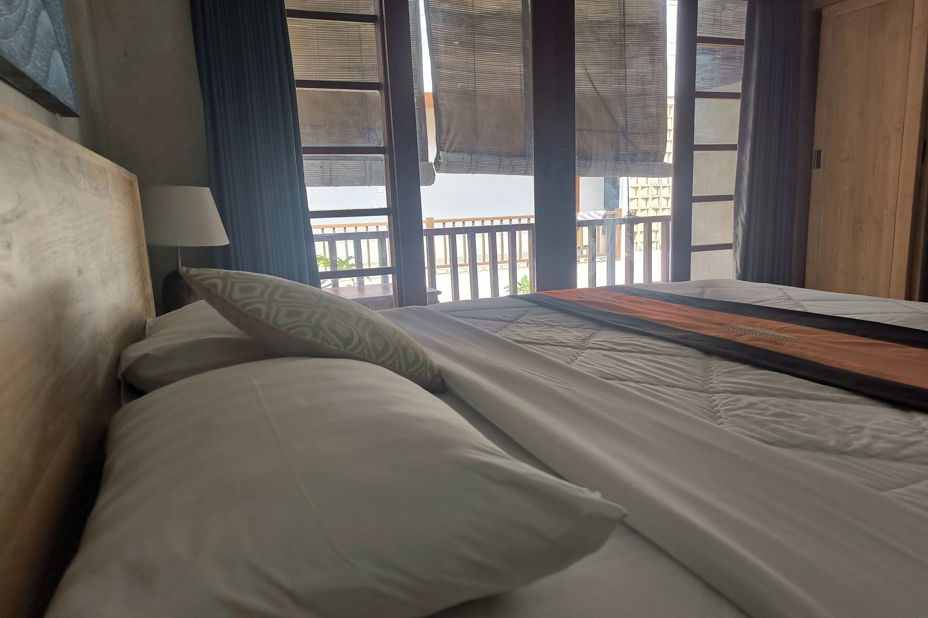 A hotel room with a bed, a nightstand, a lamp, and a view of the balcony.