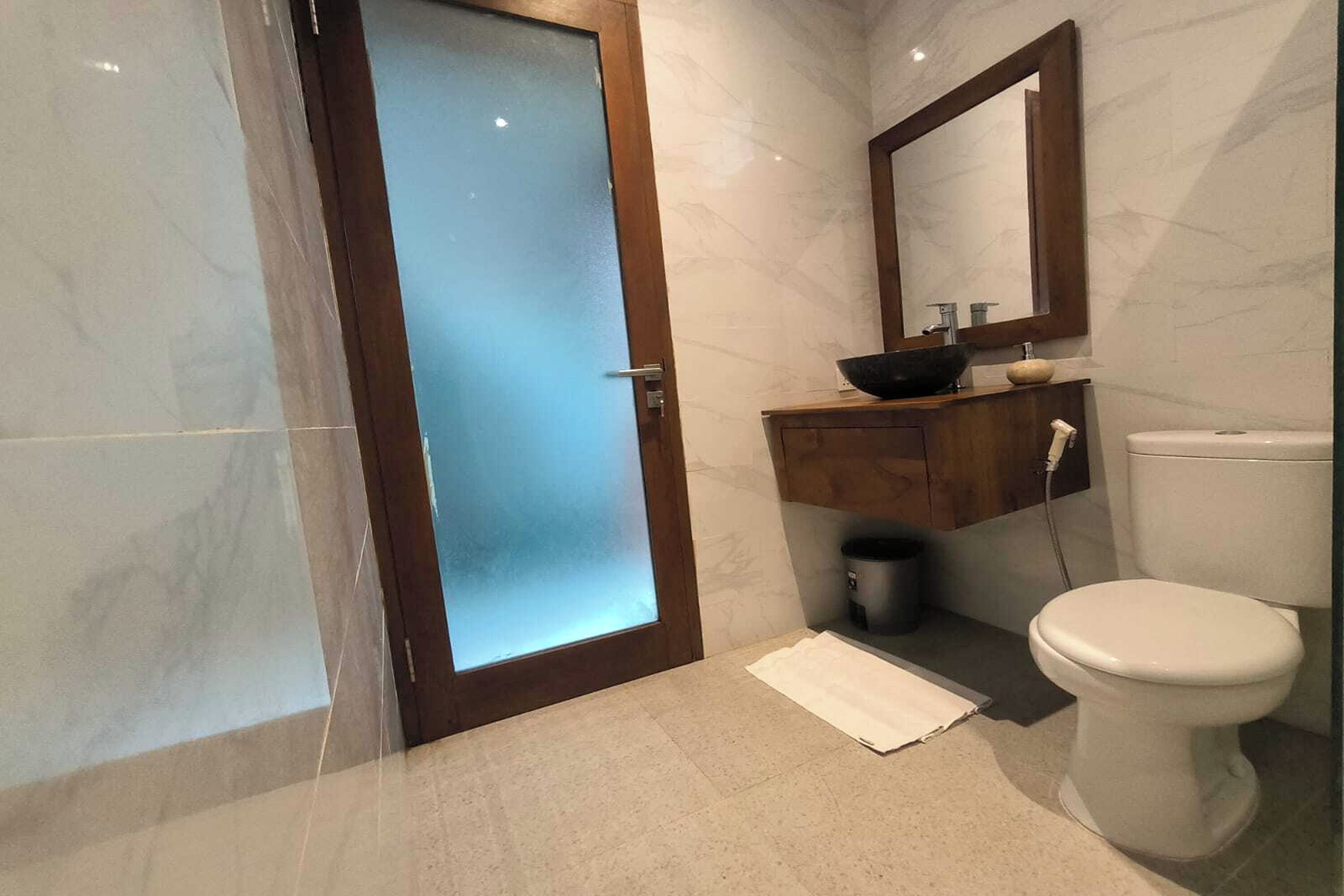 A bathroom with a wooden door, a white toilet, a wooden vanity with a sink, and a mirror above the vanity.