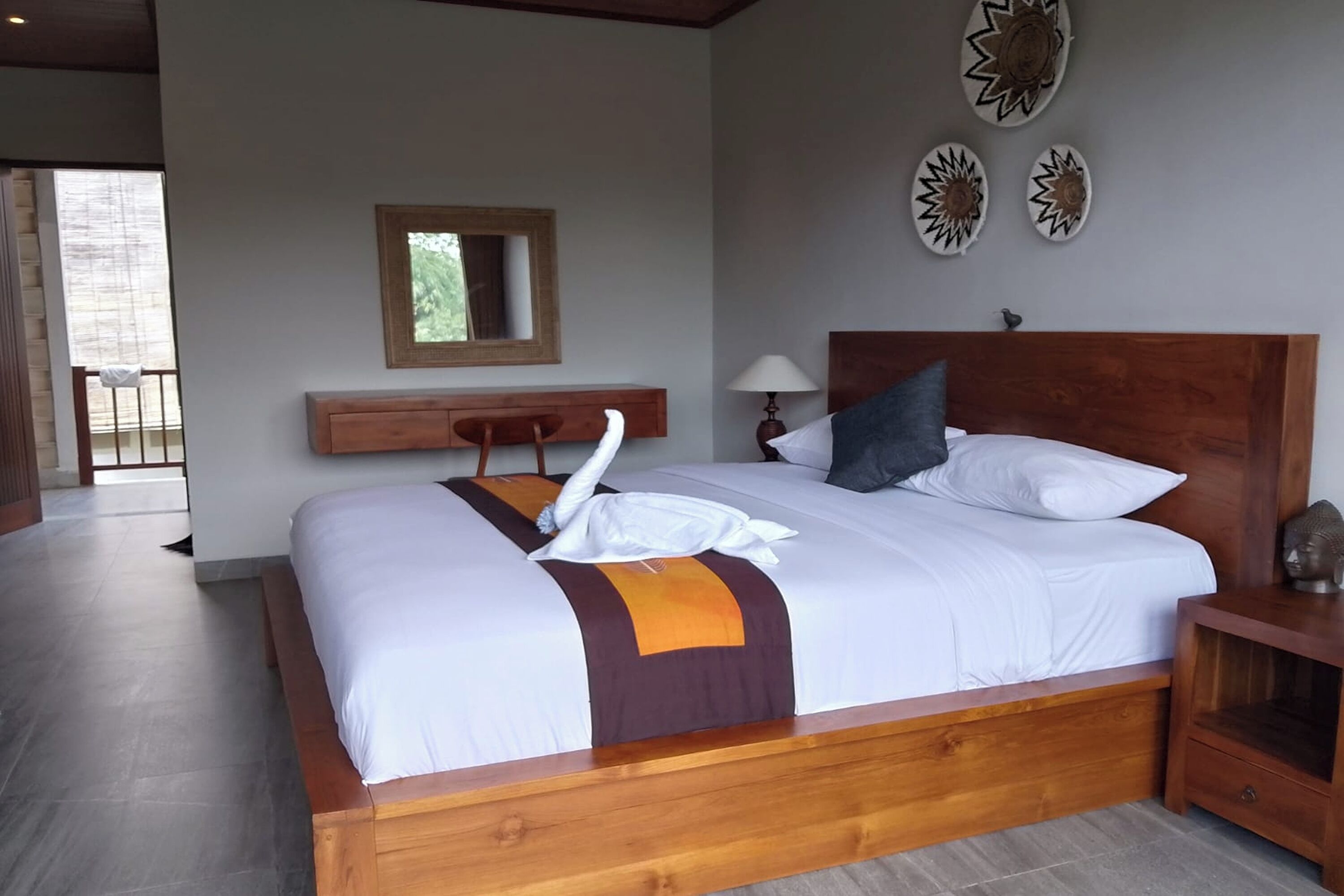 A neatly made bed with a wooden headboard, a bedside table, and a wall-mounted mirror.