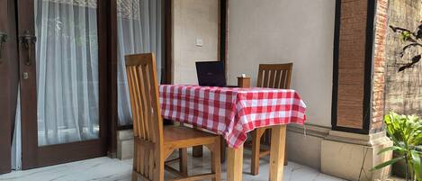 Una mesa de madera con mantel a cuadros rojos y blancos, dos sillas de madera y una computadora portátil sobre la mesa.
