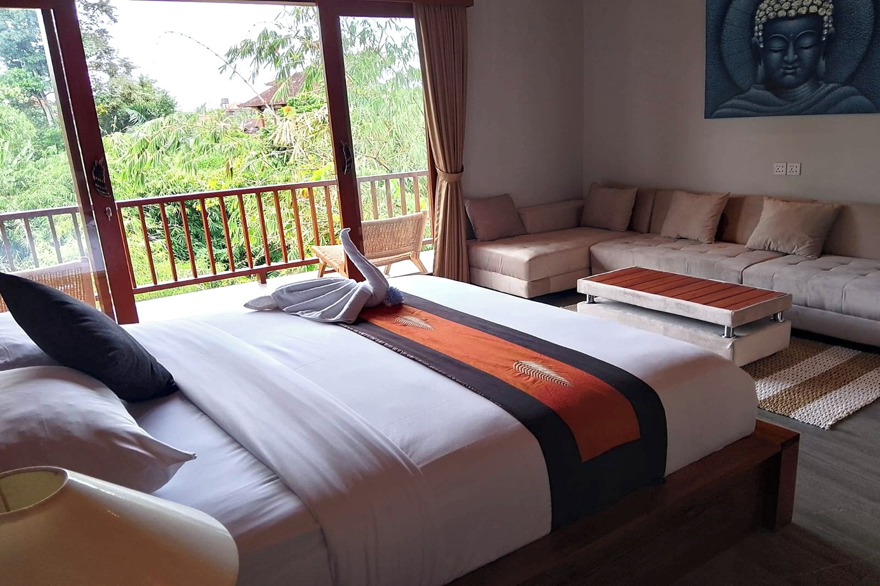 A hotel room with a bed, a sofa, and a view of greenery.