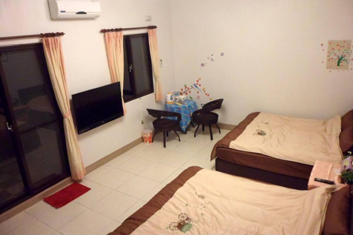 A room with two beds, a TV, a desk with a chair, and a window with curtains.