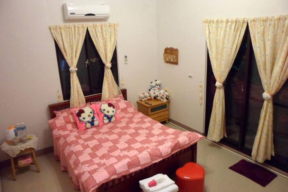 A bedroom with a bed, a nightstand, a window with curtains, and an air conditioning unit.