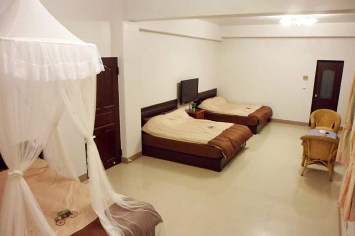 A room with two beds, a TV, a chair, and a wardrobe.
