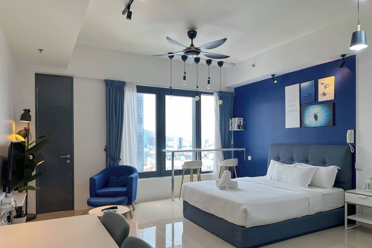 A modern hotel room with a large bed, a ceiling fan, a view of the city, and a blue accent wall.