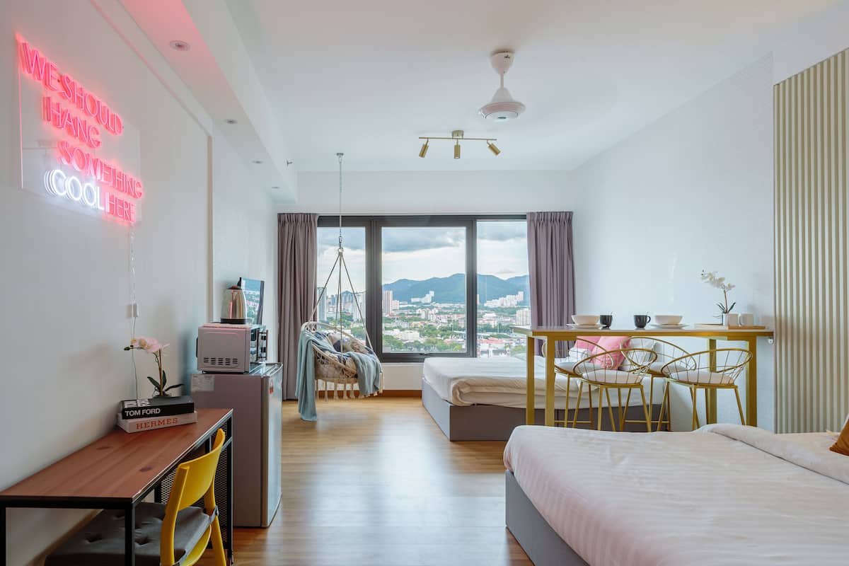 A modern hotel room with a large window, a bed, a desk, and a dining area.