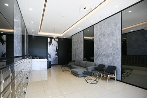 A modern hotel lobby with a glass partition, a reception desk, a grey sofa, two armchairs, and a chandelier. - Tropicana 218 Macalister (George Town)