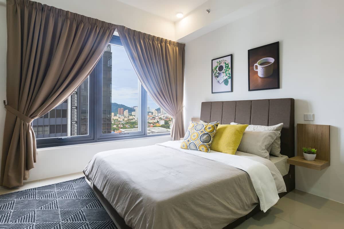 A modern hotel room with a large bed, a view of the city, and a small bedside table with a plant.