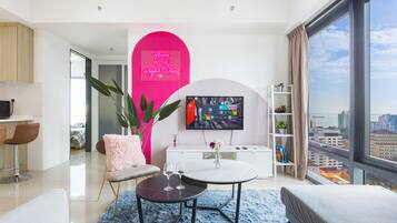 A modern living room with a large TV, a pink accent wall, and a city view.