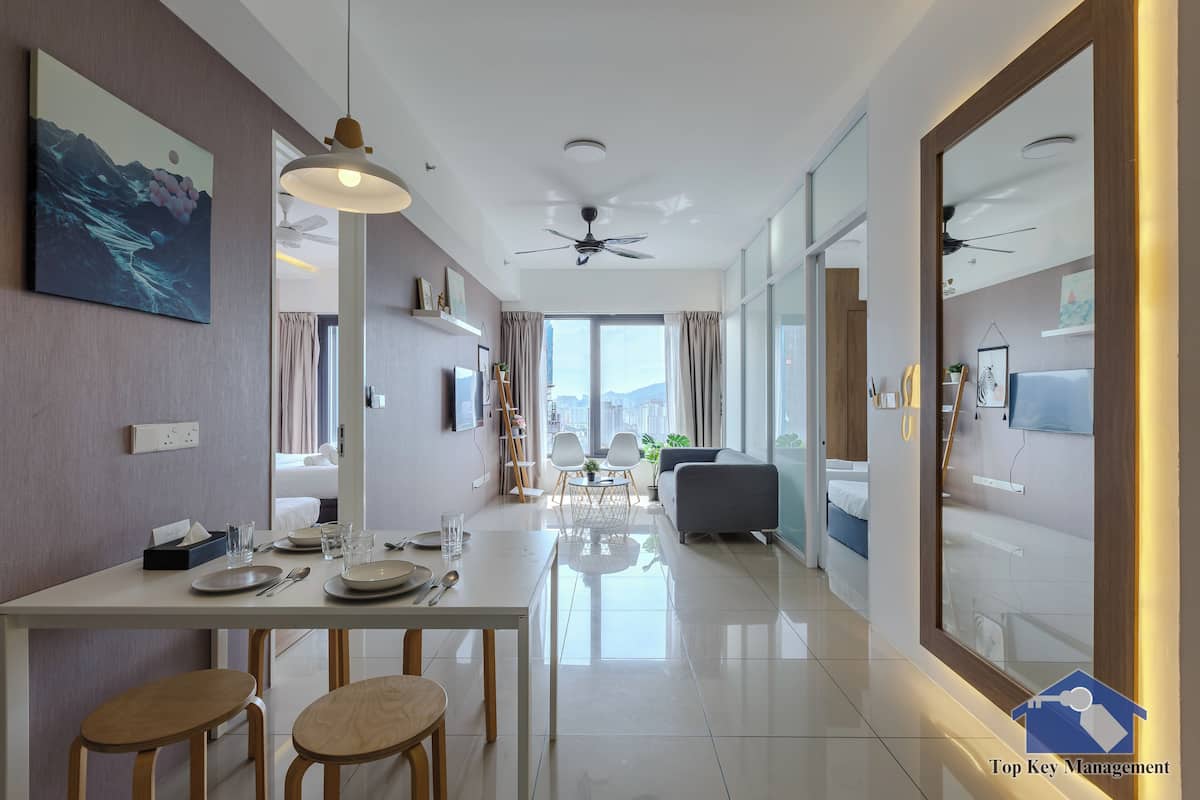 A modern hotel room with a dining area, a sofa, a TV, and a large window offering a city view.