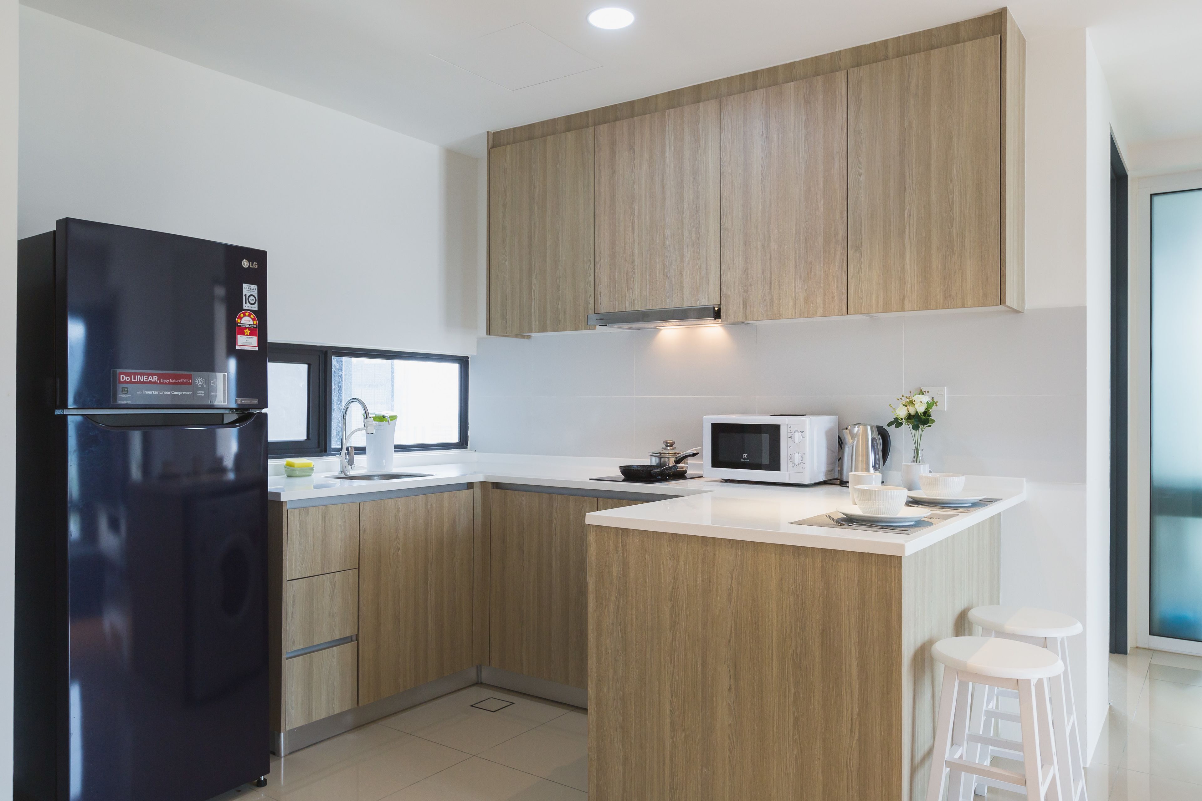 A modern kitchen with wooden cabinets, a black refrigerator, a microwave, and a small island with stools.